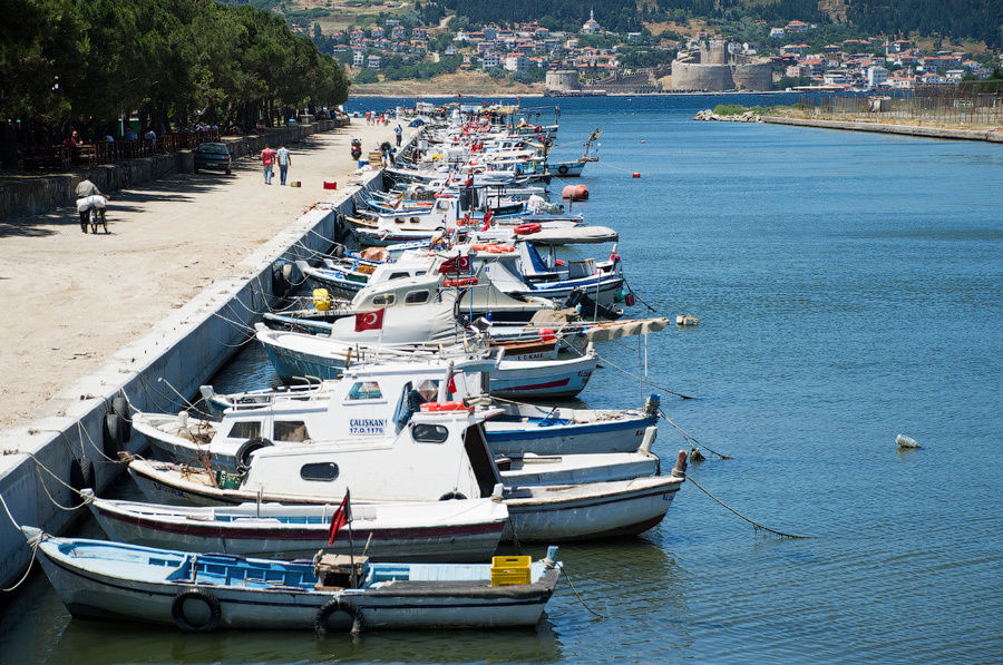 Рыбацкие лодки у берега канала и крепость на противоположном берегу пролива. Чанаккале, Турция