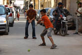 Дети играют в крикет на заставленной машинами улице