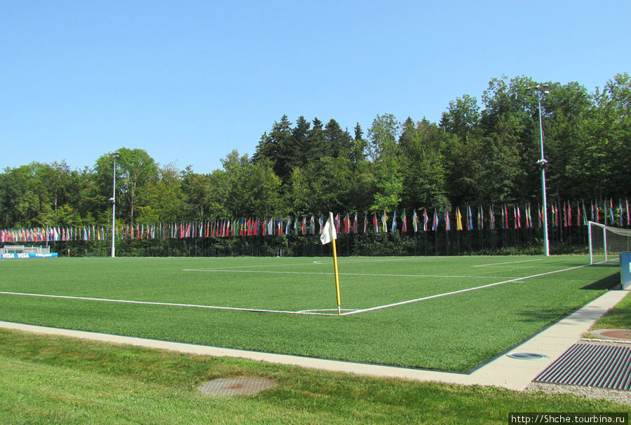 Справа от помещения поле с искусственным газоном и флагами всех государств — членов ФИФА Цюрих, Швейцария