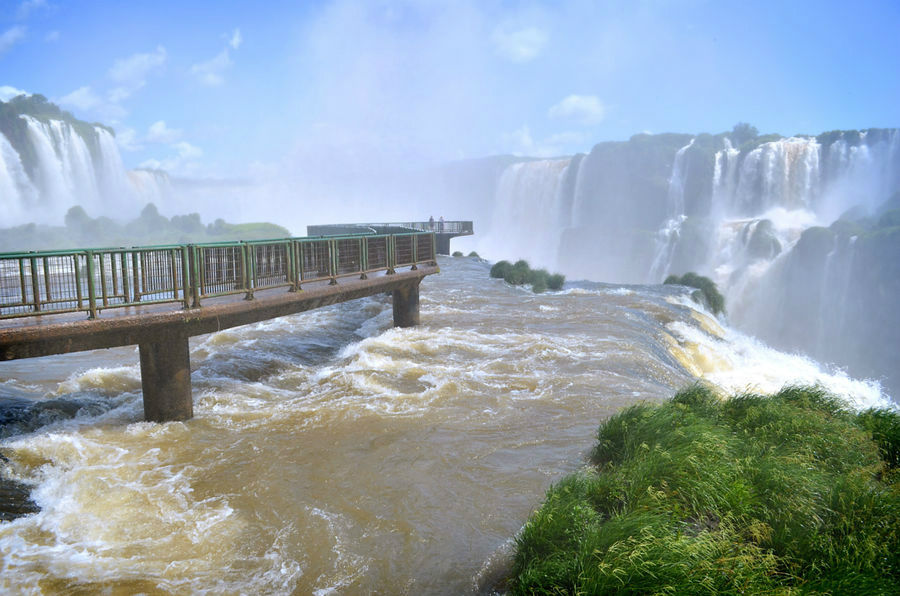 А мы уже у начала мостков, ведущих в саму ревущую Глотку! Даже сюда начинают долетать первые брызги воды, а люди начинают судорожно доставать разноцветные дождевики и закутывать фотоаппараты в полиэтиленовые пакеты! Игуасу национальный парк (Бразилия), Бразилия