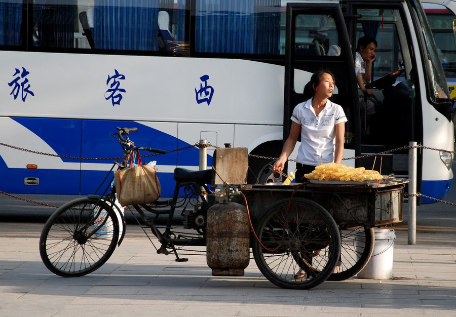 А это девушка продавец на колесах и на заднем плане наш автобус ждет около входа в парк. Линьтун, Китай