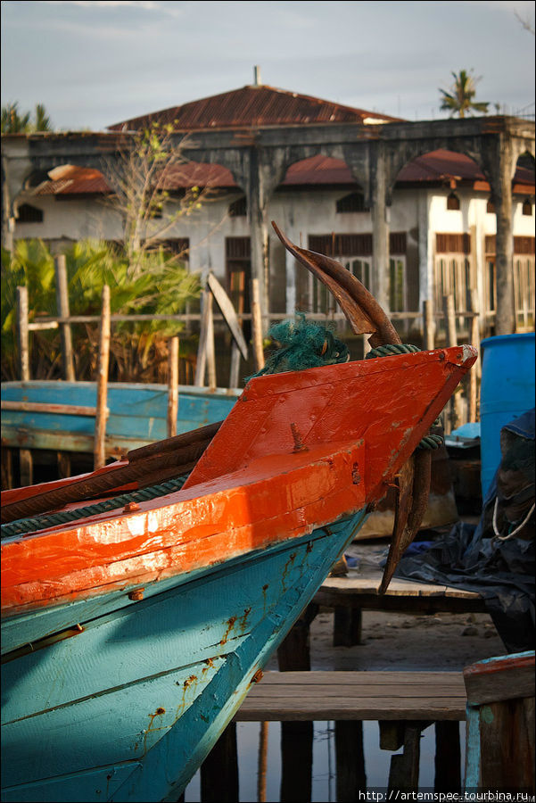 Яркая и контрастная раскраска судов жизнеутверждающе выглядит на фоне заброшенных и затопленных построек старого порта. Сингкил, Индонезия
