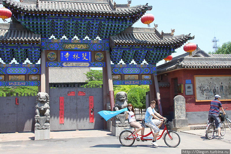 На двойном велосипеде с флагом Турбины у входа в монастырь Шуанлиньсы Пинъяо, Китай