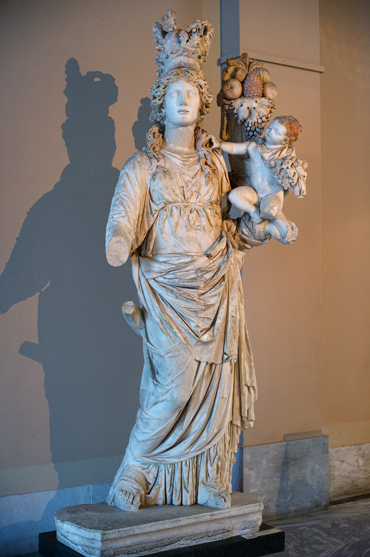 Богиня Тихе. Одета в корону, украшенную листьями оливы. В левой руке она держит рог изобилия с различными фруктами и ребенка по имени Плутос — символ богатства. Тихе является дочерью Океана. Она богиня судьбы, удачи и успехов. Богиня Тихе. Одета в корону, украшенную листьями оливы. В левой руке она держит рог изобилия с различными фруктами и ребенка по имени Плутос — символ богатства. Тихе является дочерью Океана. Она богиня судьбы, удачи и успехов.