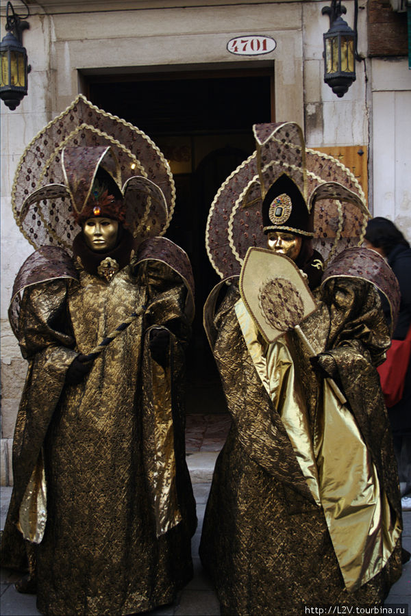 Маскеры в полных масках, дефилирующие по улочкам, фотающие друг друга и с туристами Венеция, Италия
