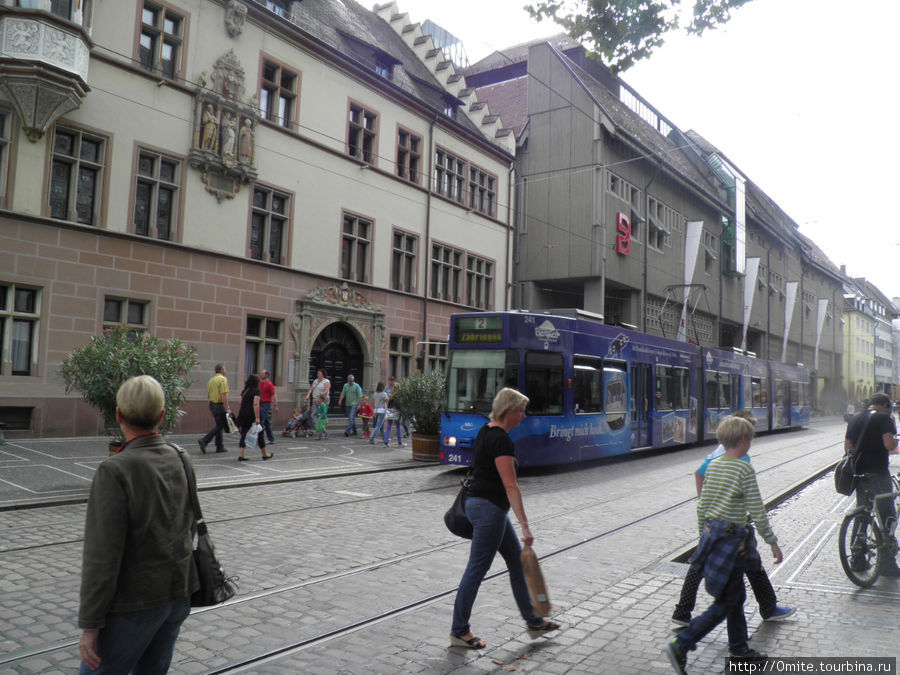Пройдя несколькими очаровательными переулками, мы вышли на Кайзер-Йозеф-Штрассе. Улица шумит: звенят трамваи, гул многоязычных групп туристов, по обе стороны множество магазинов. Фрайбург-им-Брайсгау, Германия