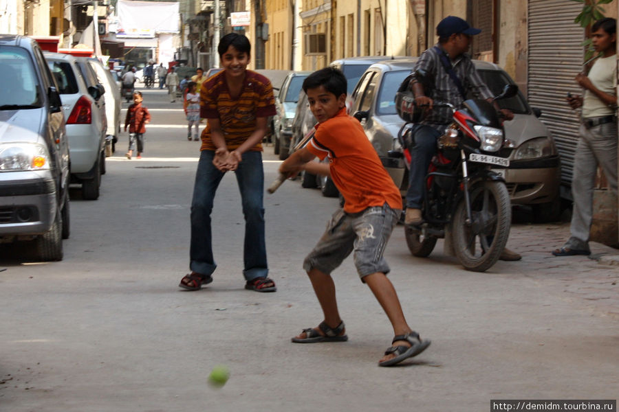 Дети играют в крикет на заставленной машинами улице Дели, Индия
