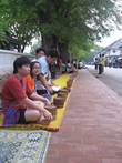 По утрам добродетельные буддисты-миряне садятся вряд вдоль улицы приготовив подношения монахам.