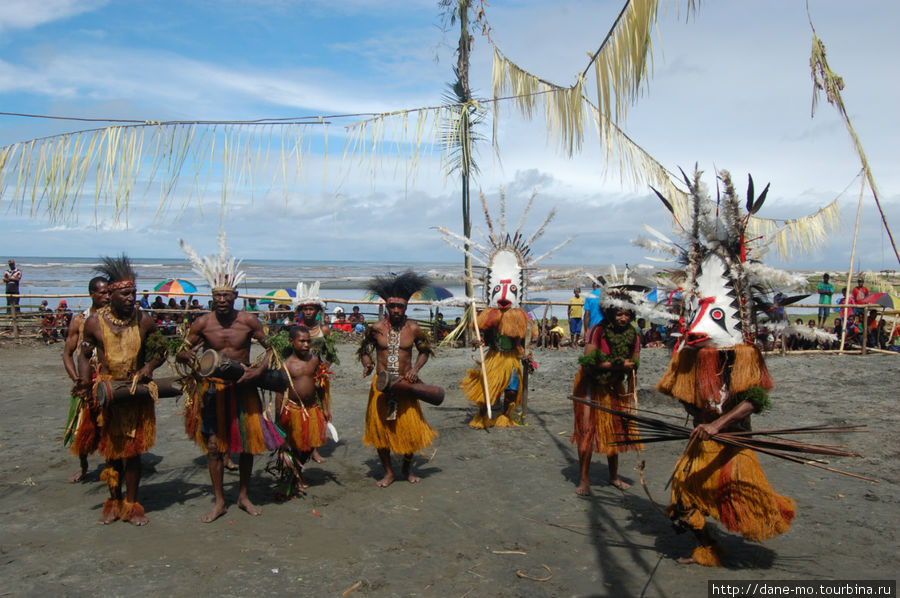 Три мужчины бьют в барабаны и поют, две маски танцуют, остальные тоже на подтанцовке Провинция Галф, Папуа-Новая Гвинея