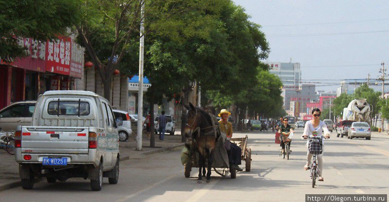 На фоне современного города можно кроме машин можно увидеть велосипедистов и запряжённую арбу Пинъяо, Китай