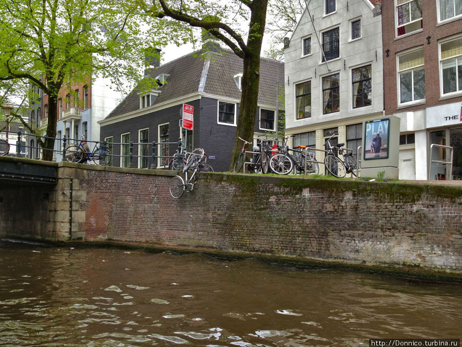 ветер, а возможно и чья-то неосторожность могут опрокинуть множественно припаркованные на набережной велосипеды прямо в канал Амстердам, Нидерланды