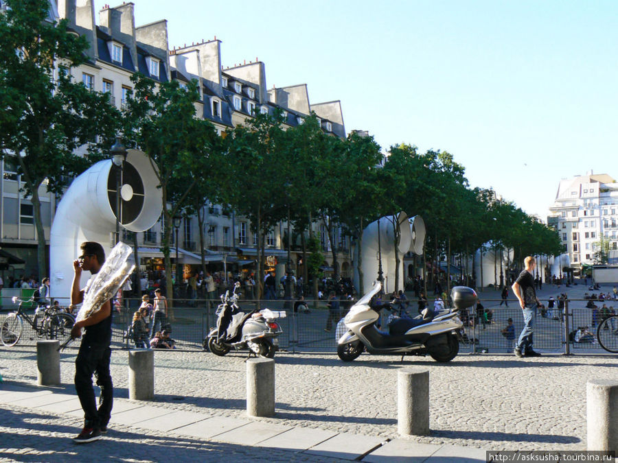 У Центра Помпиду всегда оживленно — туристы и парижане любят проводить тут большую часть времени своего свободного дня. Они прогуливаются по магазинам, сидят на асфальте, наблюдая за клоунами и жонглерами, заходя время от времени в кафе и булочные. Париж, Франция