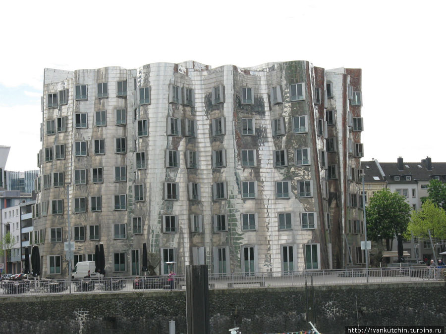 В зеркальных стенах центрального здания, как в алюминиевой банке, отражаются корпуса соседних зданий — белого и красного Дюссельдорф, Германия