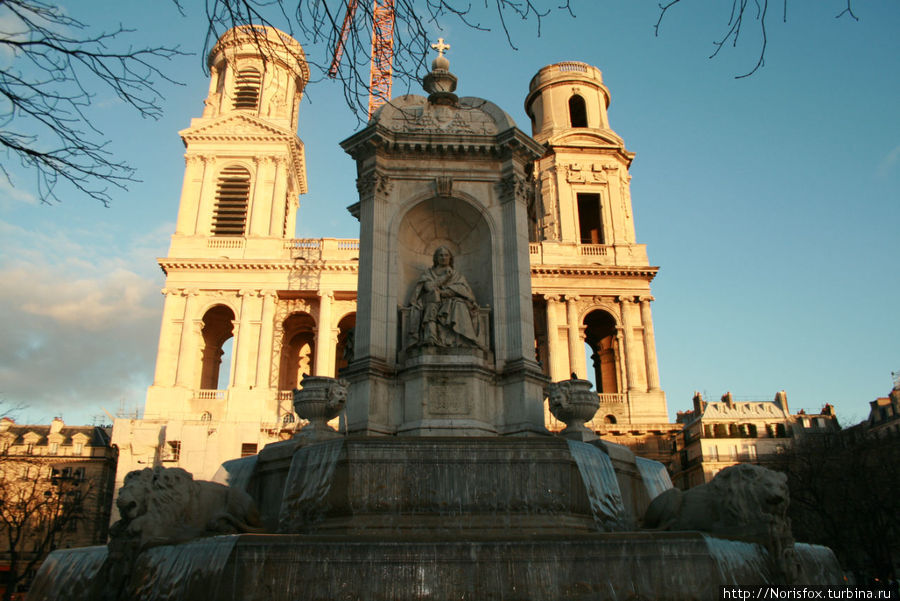 Фонтан, функционирующий, несмотря на зимний период, на фоне церкви Сен Сюльпис Париж, Франция