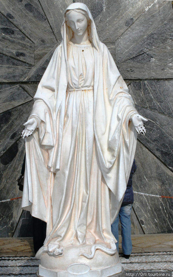 Дева Мария предстаёт перед нами во всей непорочности своего юного возраста, одетая в будничное, скромное платье, раскинувшая руки в типично иудейском приветствии-приглашении. Назарет, Израиль