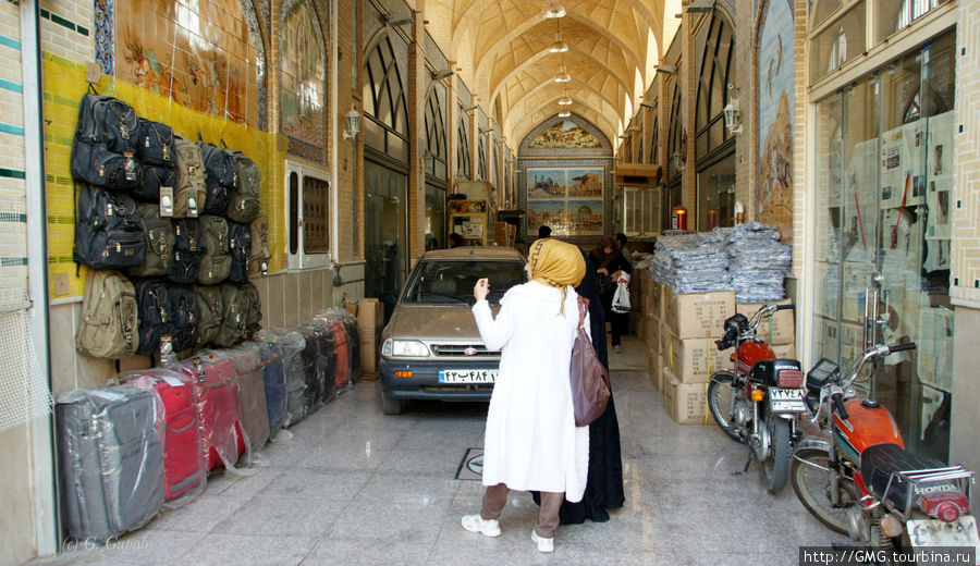 Базар — это бесконечно длинная галерея по всему периметру площади Имама. Но есть и отдельное строение. В данном случае мы видим лавки вдоль галереи. Женщины присматривают себе дешевые китайские дорожные сумки. Тут же ездят машины и мотоциклы. Последние на огромной скорости. Хотя ездить там нельзя. Исфахан, Иран